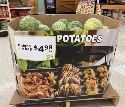 Photo of a large cardboard box in a supermarket. The box has prints of images of potato dishes and the word potato on it. A large sheet of paper with a price tag reads “onions 5lbs bag”. The box is filled with watermelons.
