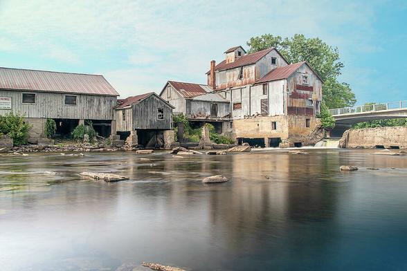 The historic Chishom Mill, in operation since the mid 1800s, sits by the glassy waters of a river on a beautiful sunny day in Chisholm, Ontario.