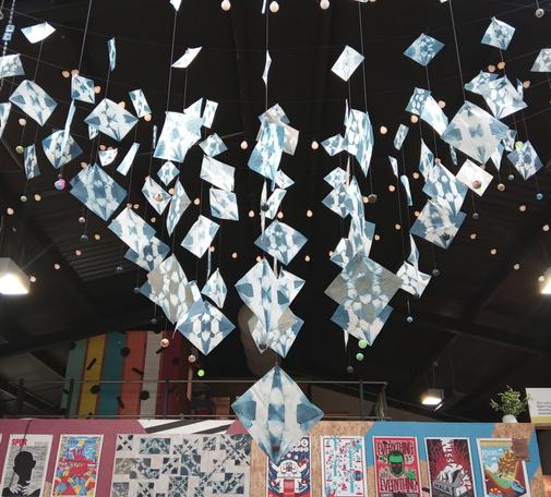 hung installation of blue and white geometrically patterned square images. about 100 of them are hung to create an inverted pyramid
