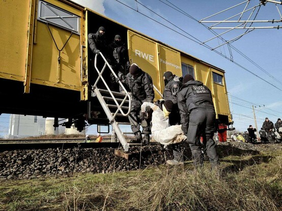 Ein*e Klimaaktivist*in wird gegen Ihren*seinen Willen von vermummten Polizist*innen in einen RWE-Zug gebracht