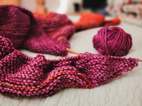 A shawl in progress, spread out haphazardly on the bed, with the focus on the working end