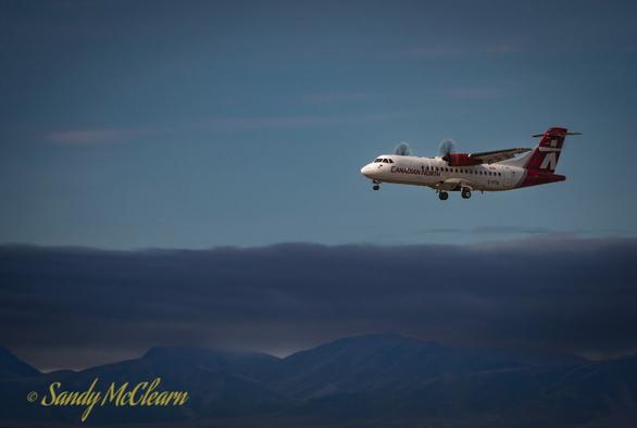 Airplane approaching the runway with gear down and cloud and blue sky in the background.