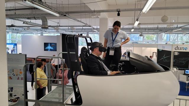 Bavarian State Minister Dr. Florian Herrmann at the VFS-TUM exhibit stand, flying the FSD flight simulator with VR googles under the guidance of TUM graduate research students. The monitor shows his view from the virtual cockpit. (VFS photo CC-BY-SA 4.0)