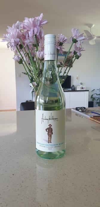 A bottle of Audrey Wilkinson Semilllon Sauvignon Blanc in front a glass vase filled with purple flowers