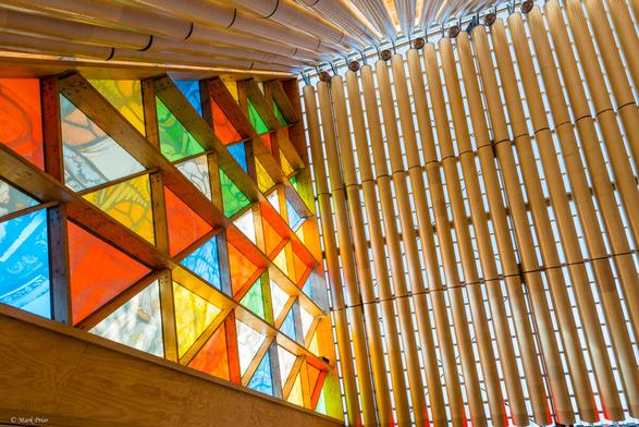 Inside the transitional cathedral. The left half of the image shows the stained glass windows, a series of multi-coloured triangular panes built into a larger triangular space.  The right side of the image show the bamboo like cardboard columns that support the A frame roof.