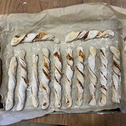 Twelve cheesy bread sticks before they went into the oven: they look pale, with gaping reddish wounds where the filling peeps through after I twisted each string of dough into its final stick shape.