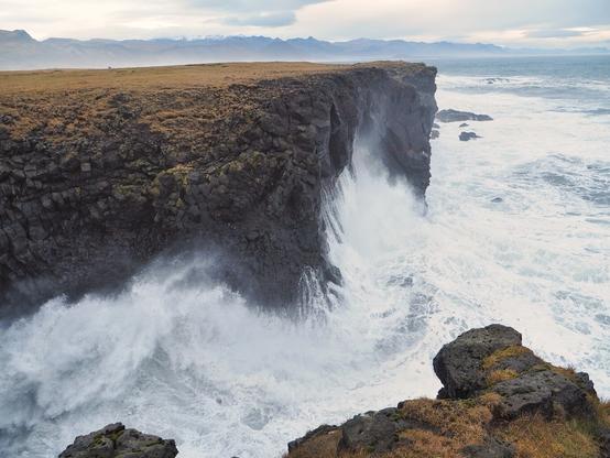 Sea cliff by a stormy sea with large waves crashing against it.