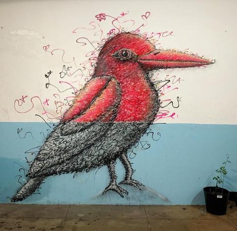 Streetartwall. On a green - white separated wall is sprayed a mural of a bird. It is executed half in gray and in the upper part in red, surrounded by small, fine graffiti dashes.