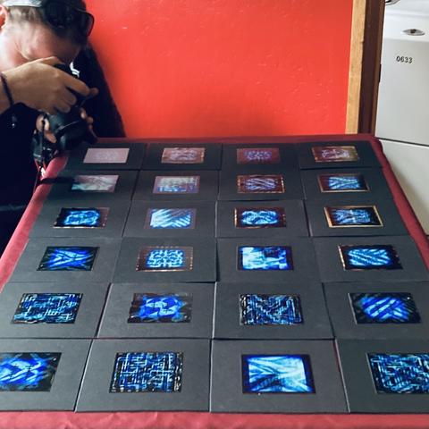 24 various record covers laid flat on a table in a grid while a photographer leans over to photograph them.