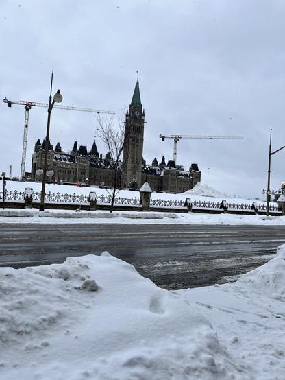 Canada’s Parliament, there is snow in front of it and there are  cranes, indicating the ongoing construction