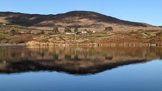 Low hills with sun and shadows on the ridge reflected in the still waters of a lake.