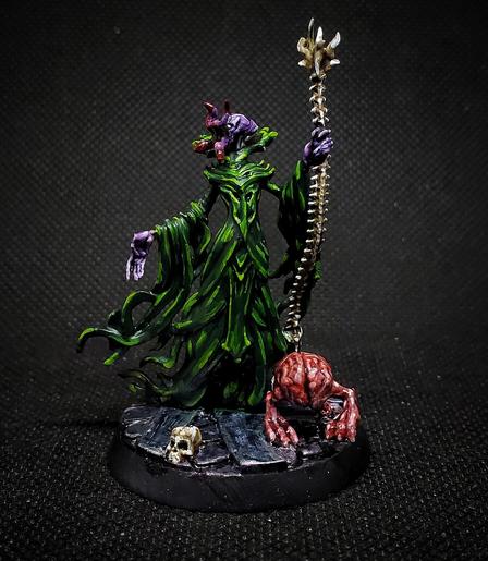 Photo of a painted miniature. A purple skinned Mind Flayer in green robes heft a spine-bone staff, accompanied by an Intellect Devourer.