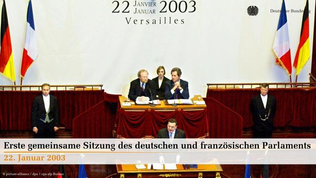 Abgebildet ist Bundeskanzler Gerhard Schröder (SPD) am 22. Januar 2003 im Schloss von Versailles in Frankreich, wie er sich an die ungefähr 900 Mitglieder der französischen Nationalversammlung und des Deutschen Bundestages, die zum ersten Mal zu einer gemeinsamen Sitzung zusammen gekommen sind wendet. Dahinter hören der damalige Bundestagspräsident Wolfgang Thierse (SPD) und der Präsident der französischen Nationalversammlung, Jean-Louis Debré zu. Im Vordergrund steht geschrieben: "Erste gemeinsame Sitzung des deutschen und französischen Parlaments. 22. Januar 2003"