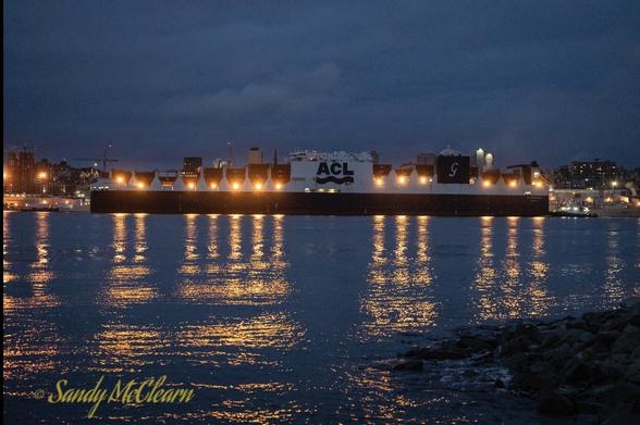 Container ship in the pre-dawn with lights reflecting on the water.