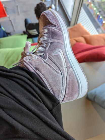 Photo of my velvet lilac Air Jodans and black jersey midi skirt resting on my knee. In the slightly blurred background are the wooden bleacher seating and cushions, along with the back of the head of a fellow event attendee.