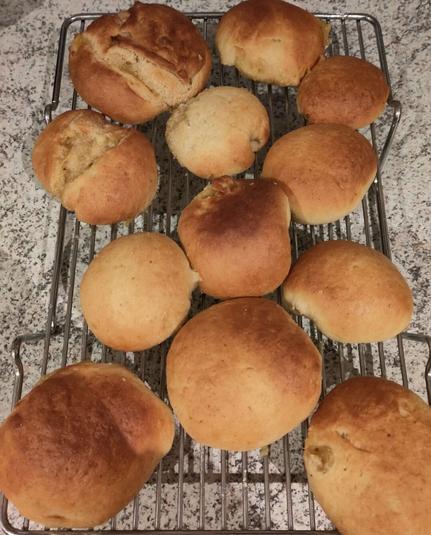 12 wheat bread rolls lightly browned on top are cooling on a metal cooling rack