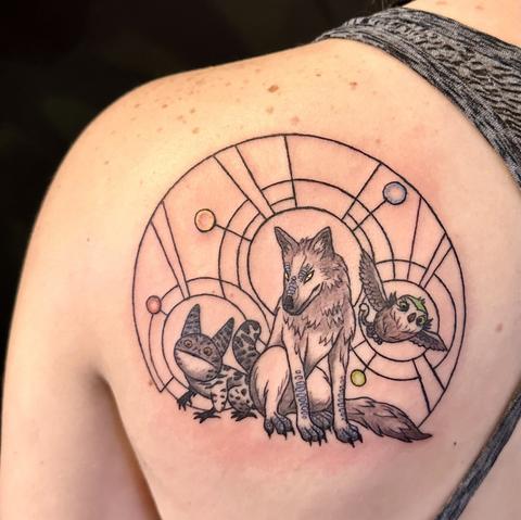 Linework tattoo on a person’s shoulder blade shows a Loth Cat, Loth Wolf, and owl surrounded by interlocking circular halos.