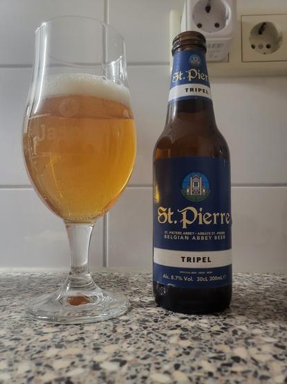 On this picture you see a glass of beer standing next to a bottle of beer with a blue label with a picture of an abbey and St.Pierre Belgian abbey beer on it