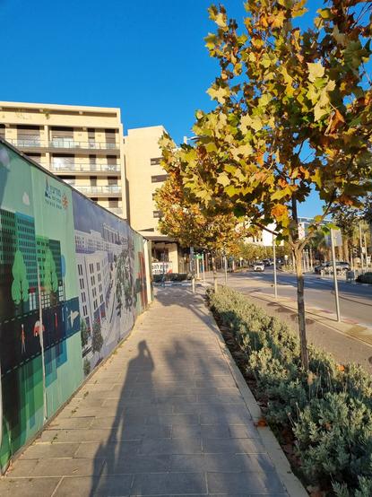 Early morning in the city center in Modiin, Israel. Tree lined walkway alongside various retail stores housed in light coloured, modern architecture.