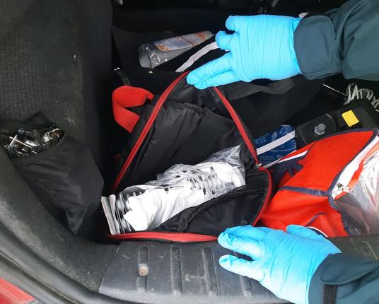 Eine schwarze Tasche mit rotem Reißverschluss wird offen gehalten. Im inneren sind zahlreiche Tablettenblister zu sehen. Die Tasche befindet sich im Kofferraumbereich eines Pkw.