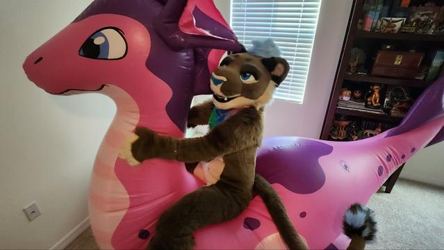 Kazi lioness fursuiter sitting on the back of a pink and purple inflatable sea dragon.