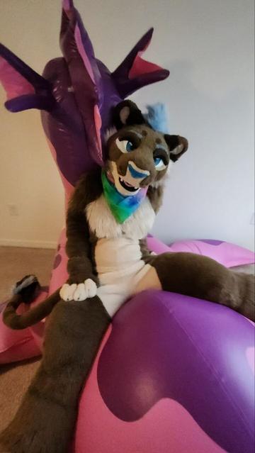 Kazi lioness fursuiter sitting on the back of a pink and purple inflatable sea dragon.