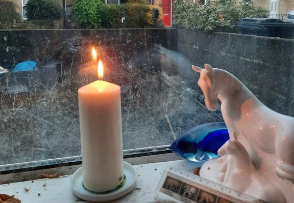 A white candle in a window. Daylight outside is fading.