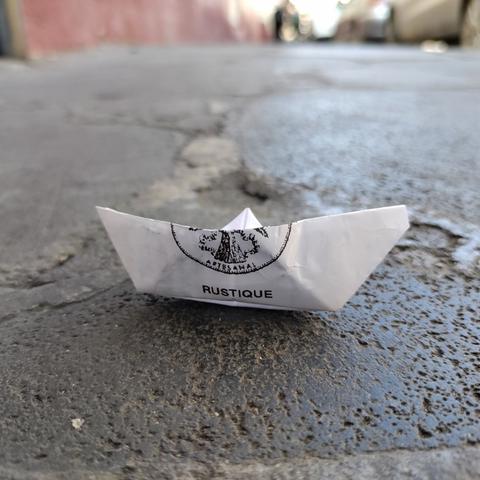 En una banqueta de Tepoztlán, un barquito de papel hecho con una hoja con la palabra "Rustique" y un logotipo impresos.