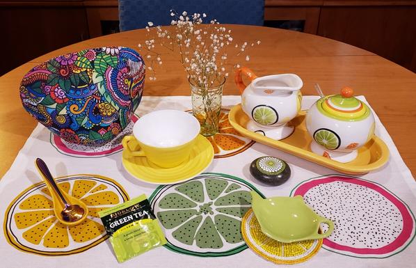 A tea tableau with a citrus fruits theme, very bright and cheery. It includes Depression-era china and glassware. The tea is Green Tea Lemon by Bigelow.