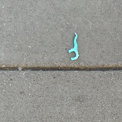 Green plastic floss pick lying on a sidewalk.