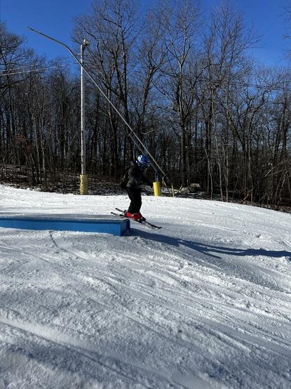 A small child jumping off of a blue metal rail on a ski slope