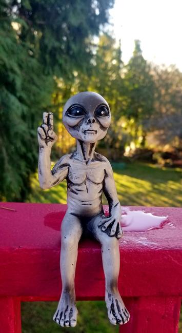 My alien figurine, flashing hand peace sign, sitting on back deck.