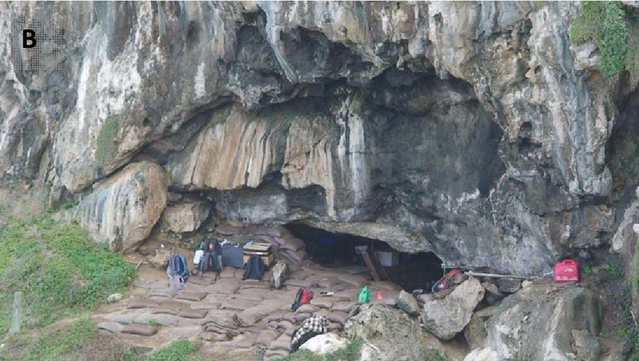Looking at the entrance of Blombos Cave, a small opening near the bottom of the photo. Sandbags and backpacks are in front of the entrance.