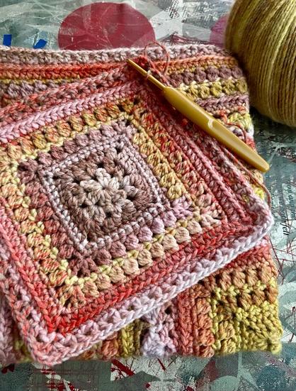 Crochet squares made from variegated wool in colours of mustard, coral, pink, taupe.