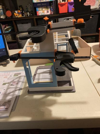 Dollhouse kit walls being glued together,held with mini bar clamps while glue dries