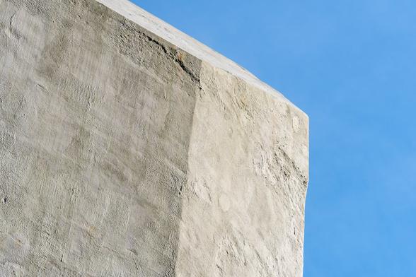 A color photograph of one corner of a giant concrete block serving as a counterweight for a bascule bridge, with a clear blue sky in the background.