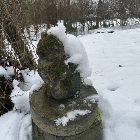 A closeup of the stone cat on my terrace. The dark grey and season-weathered cat is almost free of snow again but there's still some on its back and that bit of snow looks like some strange snow critter riding piggyback. Most of the rest of the pic is the still snow-covered grass.