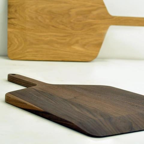 Two pizza paddles in white oak and walnut. One is propped up on its side and the other is laying flat.