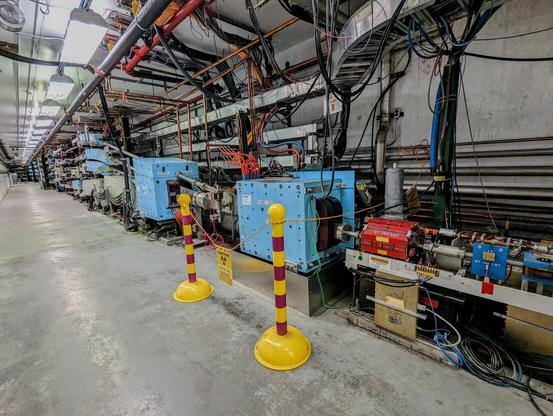 Looking Westward toward the West Arc from the end of the Spreader. One sees a series of blue dipole magnets. The closest two of these dipole magnets contain multiple passes each, and are recombining them into a single beamline, which will then go into the North Linac.