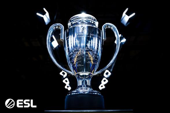 Zdjęcie trofeum - pucharu IEM Katowice, srebrny puchar z wygrawerowanym logo ESL, napisem Intel Extreme Masters i triumfatorami poprzednich edycji, ustawiony na czarnym tle
