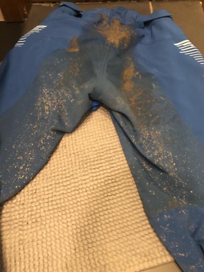 Auf dem Badezimmerboden liegt eine blaue Hose. Man sieht die Hinterseite. An GesÀà und inneren Beinen ist alles nass und mit Dreck besprenkelt, mittig zwischen SitzflÀche und Bund ist sehr viel Schlamm