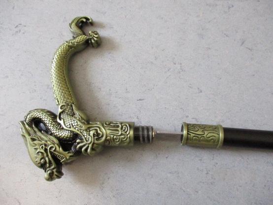 Ein Gehstock mit Drachengriff und herausziehbarer Klinge liegt auf einem Tisch.