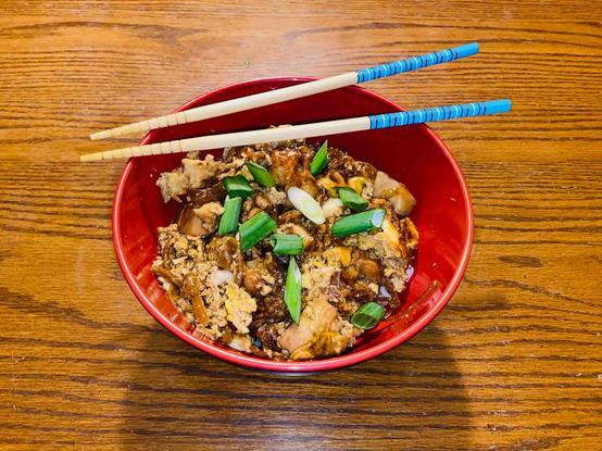 A bowl of oyakodon (chicken, egg, onion over rice) with blue chopsticks.