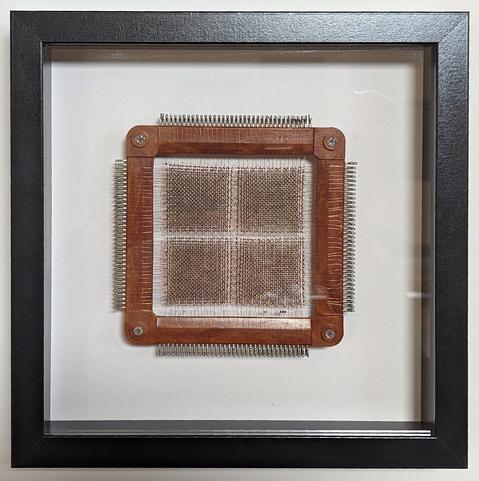 A core memory module. Size is approximately 140 X 140 mm. These are made to be stacked into a cube approximately 140 mm to a side. On this module, a grid of very fine copper wires is woven on a frame. The frame appears to be brown coloured Bakelite with soldering terminals embedded along all four sides. The strands of copper wire are as fine as a human hair. Where each copper wire crosses at a right angle, they pass through a tiny toroidal magnet. To write one bit of data, the computer applies a voltage to a specific pair of wires in a row and column. The electrical current creates a magnetic field around the wire, and the direction of the magnetic field is determined by the polarity of the current. This magnetic field gets stored in the magnet at the intersection of the wires, along with its direction. Thus, the direction of the magnetic field encodes a '0' or '1' datum in memory.