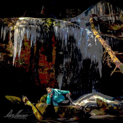 Posterized: Woman sitting in front of rock cliff with icicles melting off it. Dead tree on right.