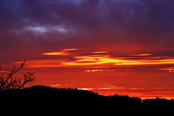 Intense crimson skies with streaks of gilded clouds are embellishing and adding dimensionality to a silhouette of an otherwise rather dull suburban landscape. This particular photo was shot at a focal length of 100mm.