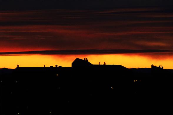Intense crimson skies with streaks of gilded clouds are embellishing and adding dimensionality to a silhouette of an otherwise rather dull suburban landscape. This particular photo was shot at a long telephoto focal length of 600mm.