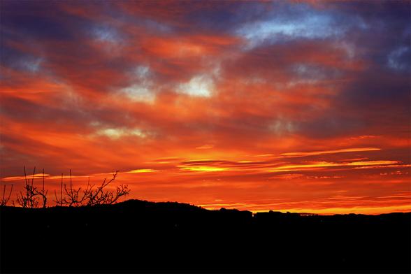 Intense crimson skies with streaks of gilded clouds are embellishing and adding dimensionality to a silhouette of an otherwise rather dull suburban landscape. This particular photo was shot at a focal length of 50mm.