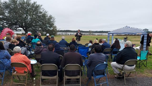 Rabbi Evan Ravski speaks to an audience outdoors, with the Ashley River in the background.