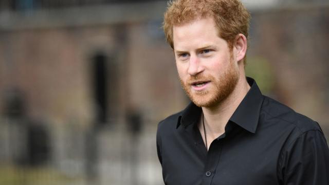 Prince Harry walking outside. He is wearing a black shirt, the building behind him is blurred. Photo credit: Shutterstock